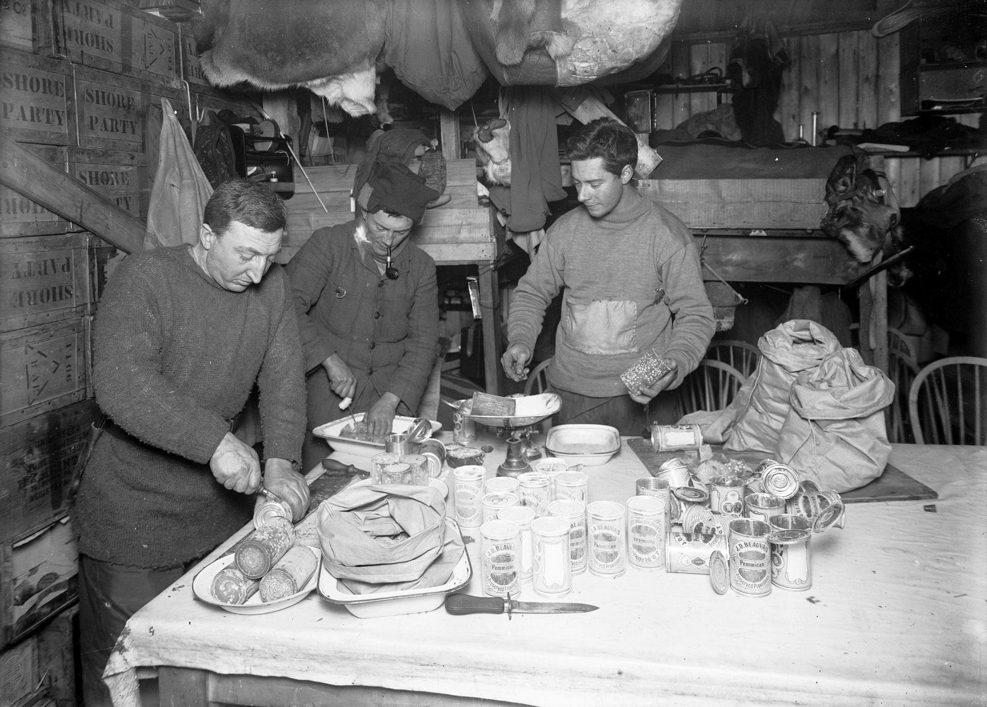 Dr Atkinson, Lieut Bowers and Mr Cherry-Garrard cutting up pemmican, June 23rd 1911.
