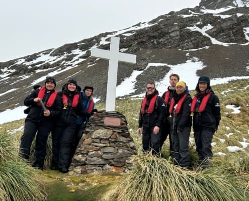L-R: Inspiring Explorers Charlie Thomas, Kaitlyn Martin, Kelly Davenport, Lawrence Rothwell, Henry Conquer, Porohu Hagai Noa and Jenny Sahng at the Hope Point memorial cross. Grytviken Antarctic Heritage Trust Inspiring Explorers Expedition