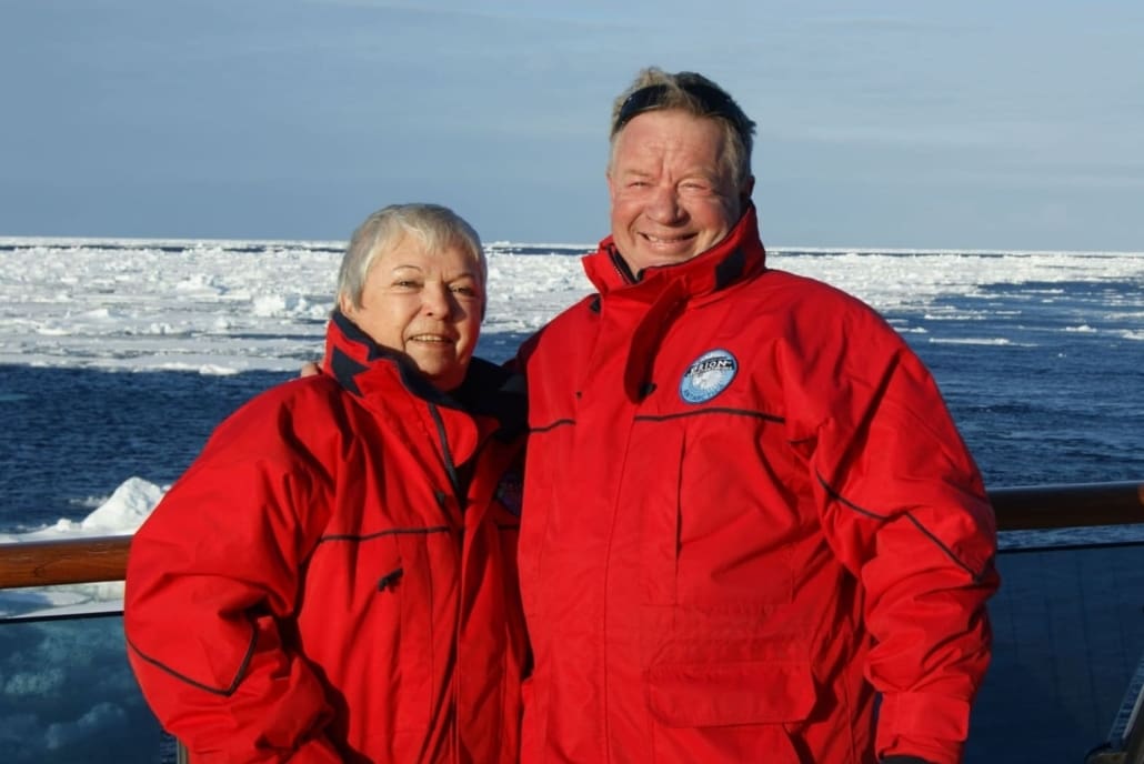 A man and woman standing against the rail of a ship with ice floating in the background.