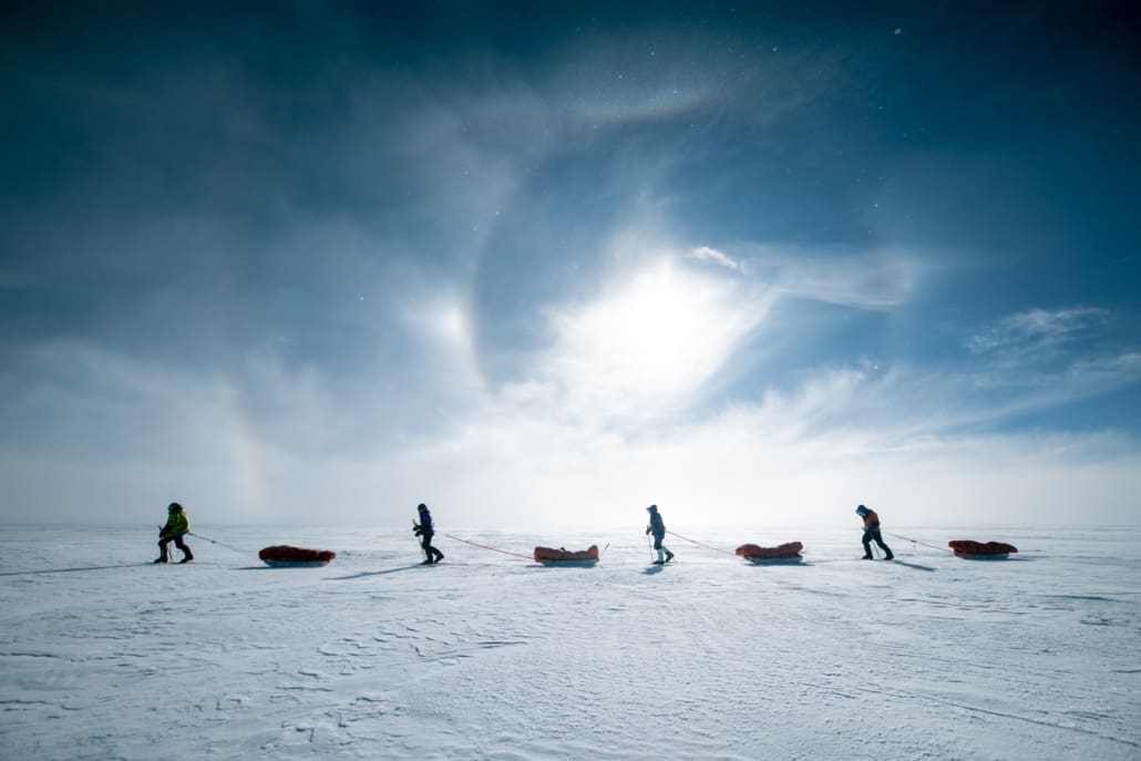Four people dragging sleds over icy terrain.