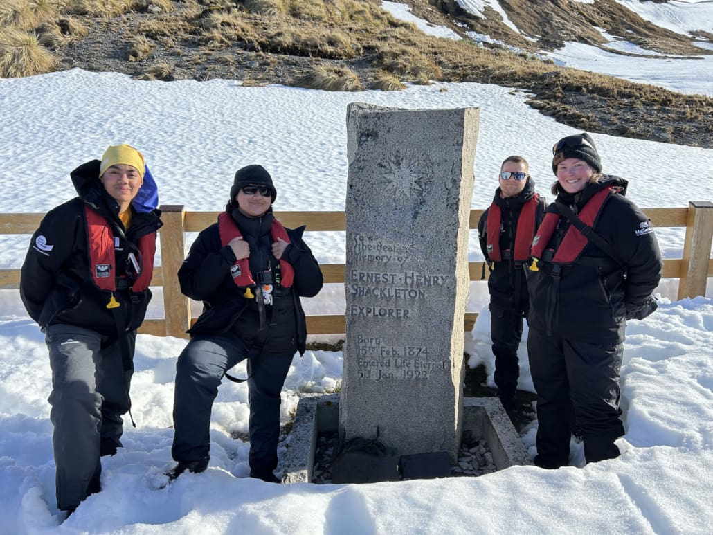 Four people standing beside the tombstone of Ernest Shackleton.