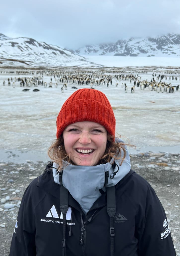 A woman in an icy landscape with penguins and mountains in the background.