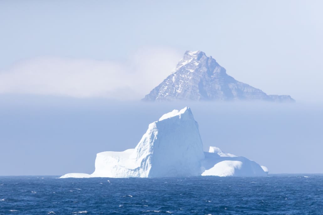 An iceberg floating in water with a mountain in the background.
