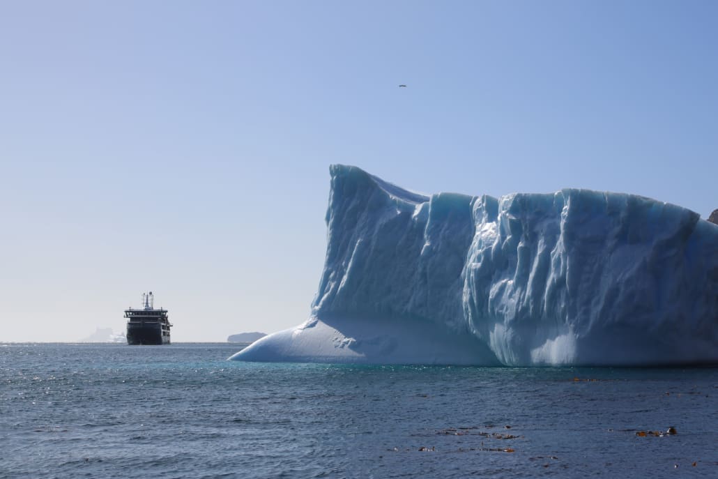 A cruise ship next to a large iceberg.