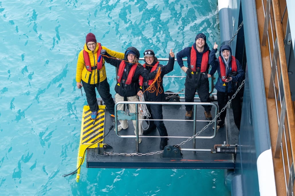 People smiling at the camera while standing on a boat gangway.