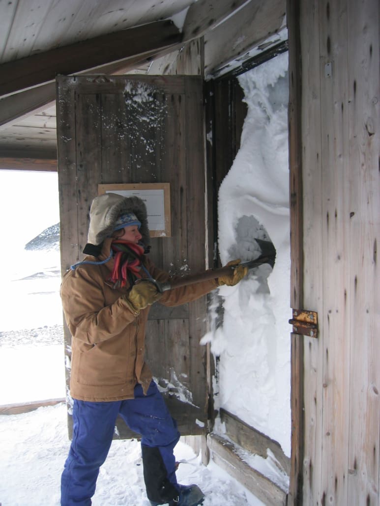 A person digging out the snow-filled doorway of a historic building in Antarctica